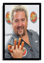 Guy Fieri framed wall art print depicts the chef smiling with spiky blond hair and fried snacks on his fingers in a black frame.