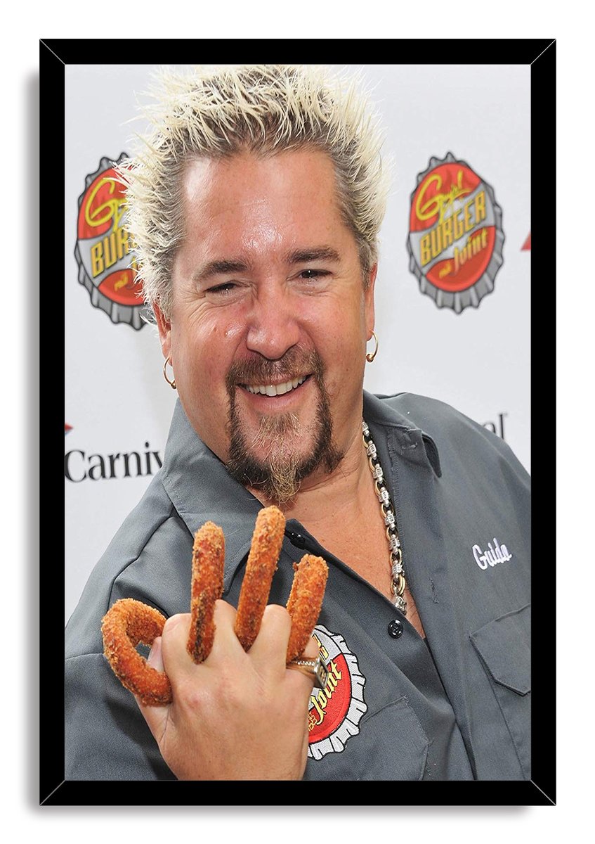 Guy Fieri framed wall art print depicts the chef smiling with spiky blond hair and fried snacks on his fingers in a black frame.