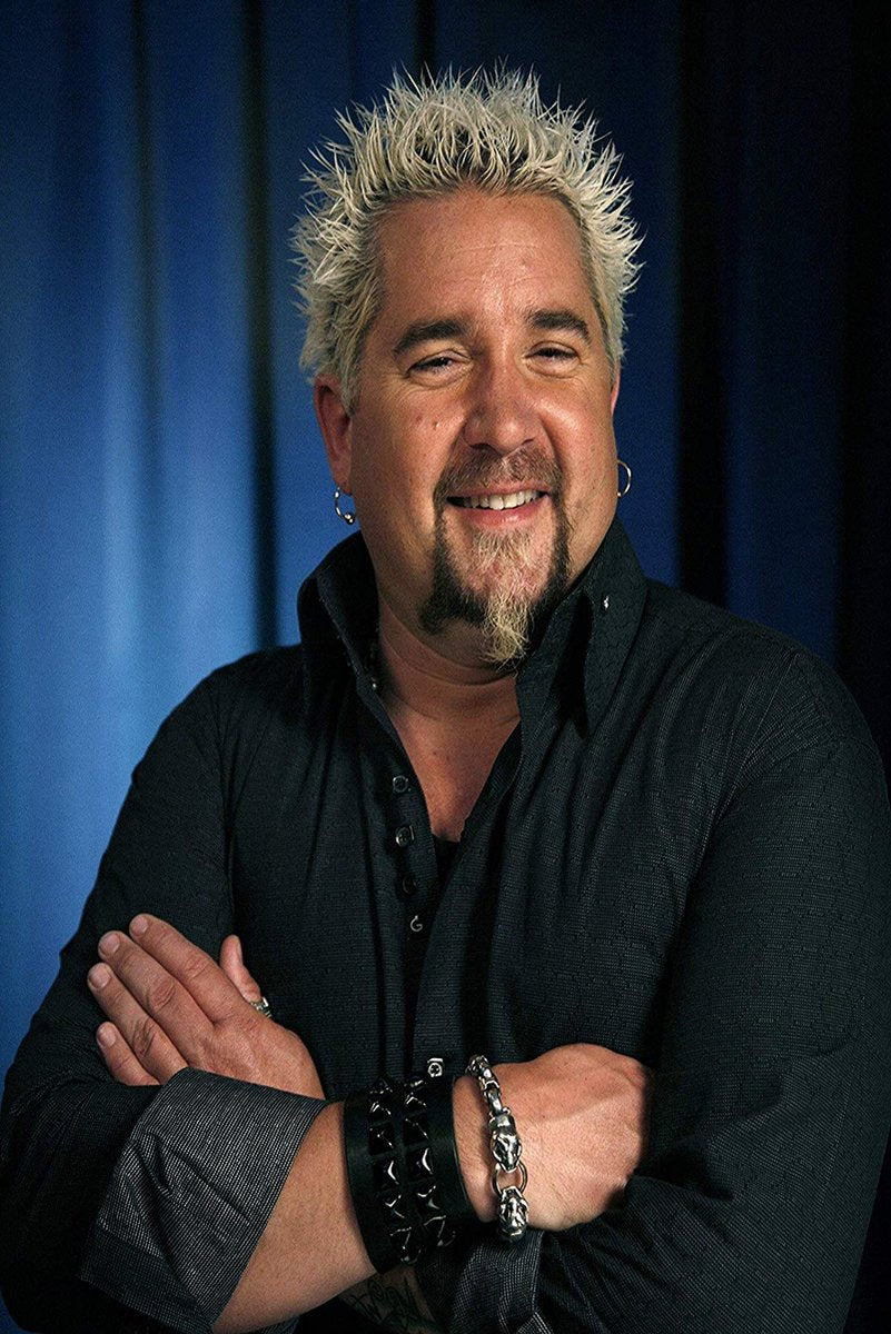 Guy Fieri wall art print features a smiling portrait with spiky blond hair, crossed arms, black shirt, and blue backdrop.