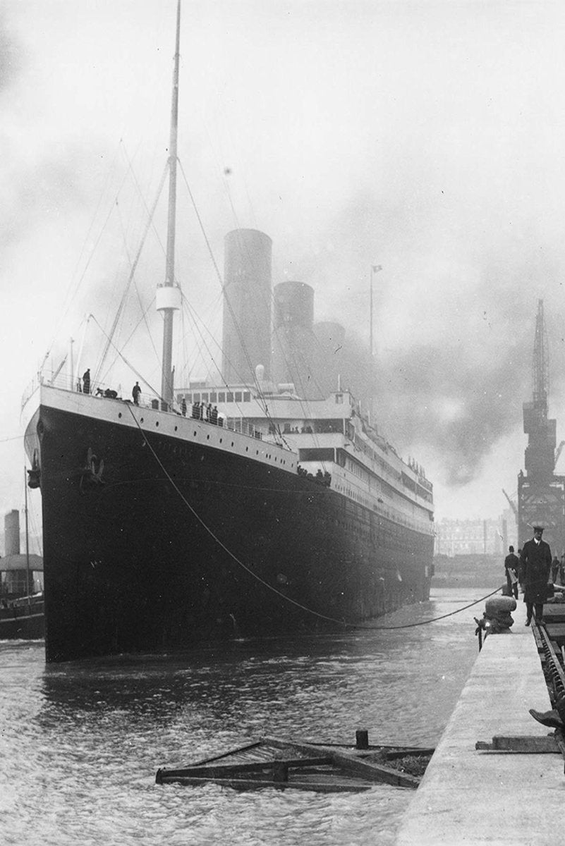 Titanic poster depicts the ocean liner moored at a dock, with towering funnels, smoke, cranes, and figures beside the water.