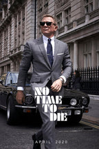 James Bond No Time To Die poster features Daniel Craig in a gray suit and sunglasses walking before a black sports car on a city street.