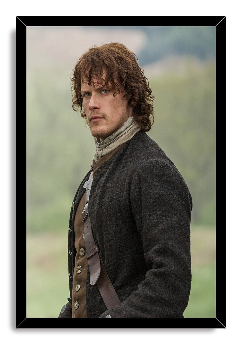 Jamie Fraser framed wall art print presents Sam Heughan in a black frame, wearing a charcoal coat, scarf, waistcoat, and leather shoulder strap.