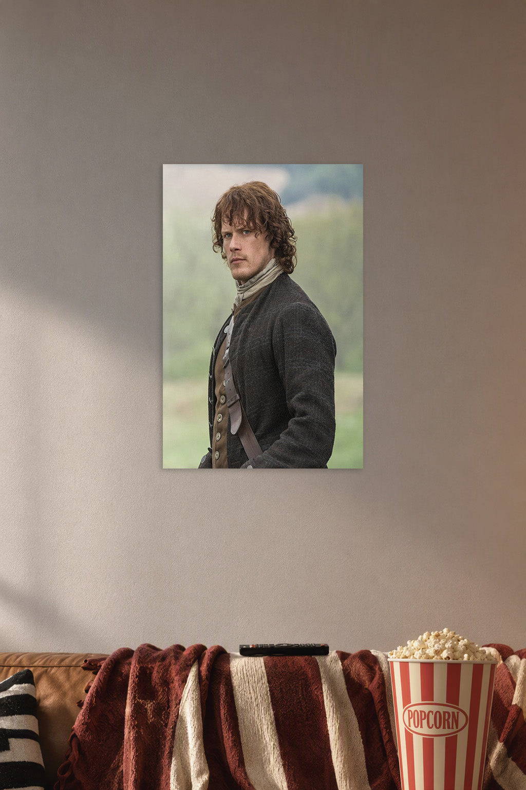 Jamie Fraser (Sam Heughan) from Outlander in a cozy movie room above a brown sofa with popcorn.