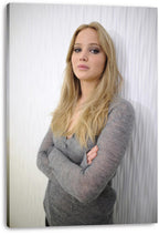 Jennifer Lawrence canvas wall art print displays a blonde woman in a gray sweater standing with crossed arms against white curtains.