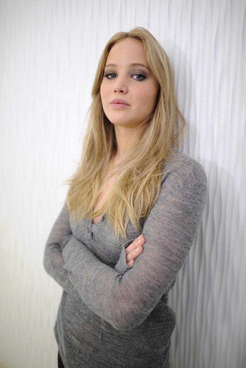 Jennifer Lawrence poster features a blonde woman in a gray knit top with folded arms before white draped curtains.
