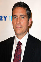Jim Caviezel poster portrait in a black pinstripe suit, white shirt, and red paisley tie against a pale event backdrop.