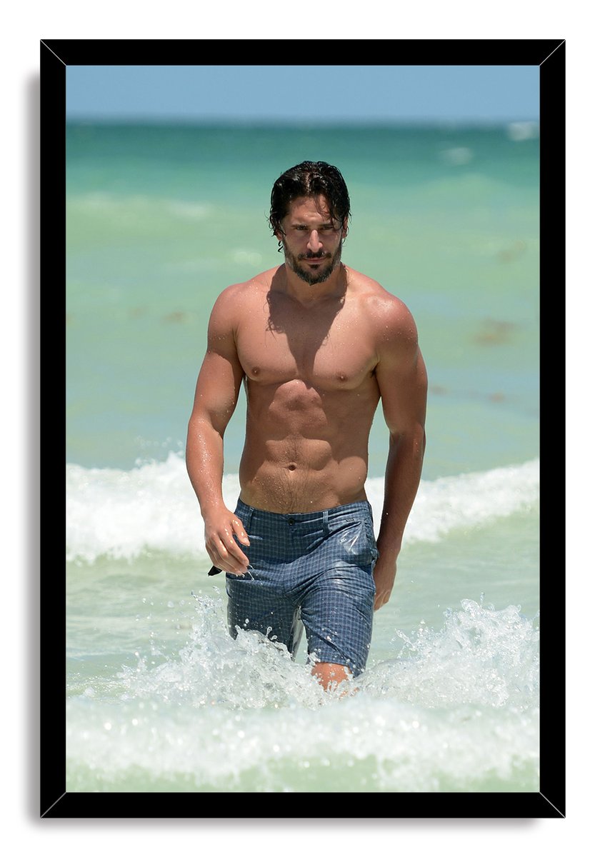 Joe Manganiello framed wall art print shows a shirtless man in blue shorts walking through breaking ocean waves.