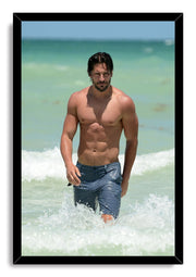 Joe Manganiello framed wall art print shows a shirtless man in blue shorts walking through breaking ocean waves.