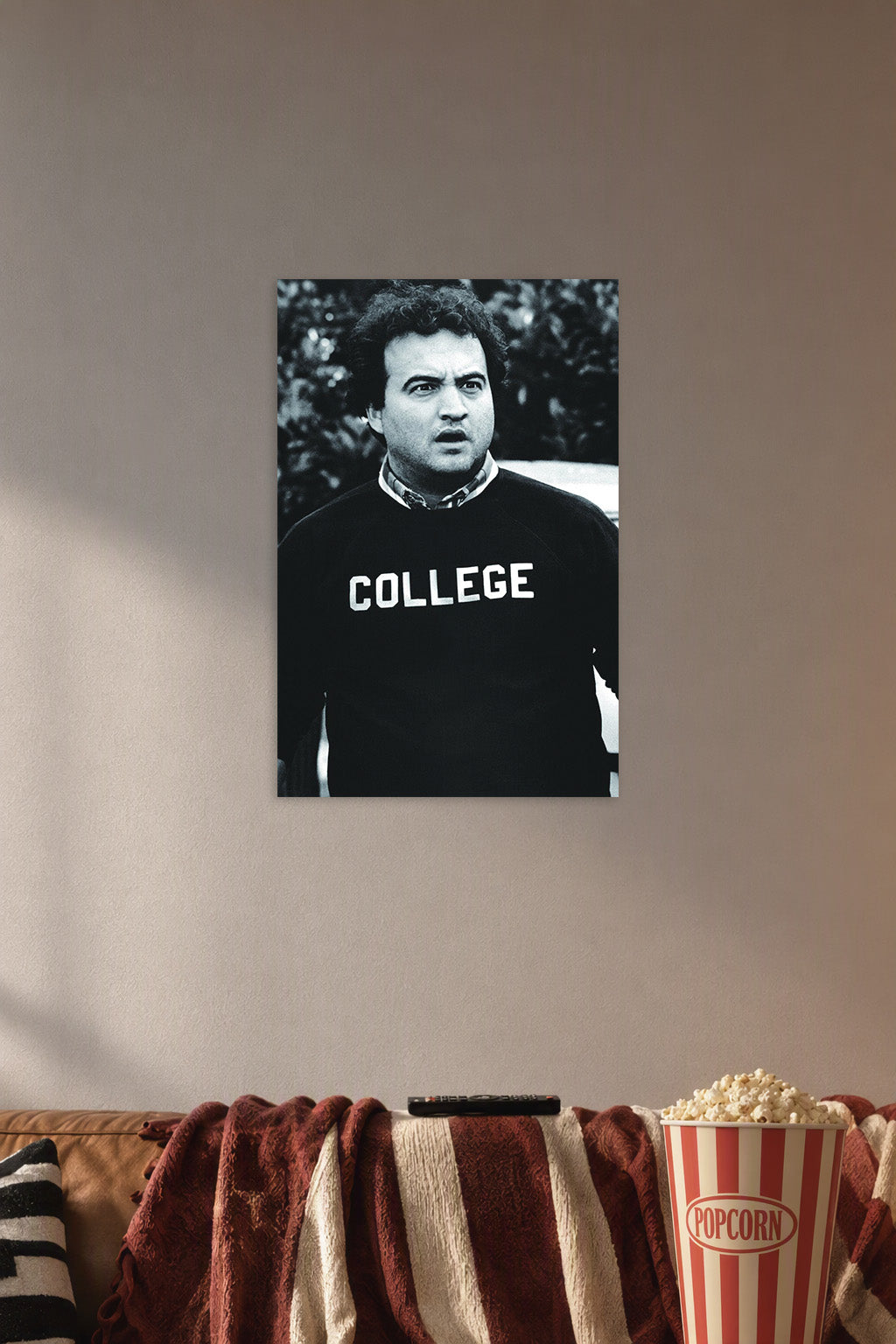 John Belushi as Bluto Blutarsky from Animal House in a cozy movie room above a brown sofa with popcorn.
