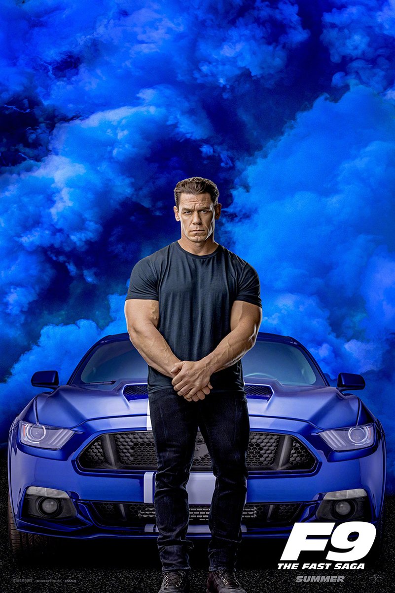 John Cena F9 movie poster with Cena standing before a blue striped muscle car beneath dramatic blue smoke clouds.