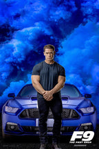 John Cena F9 movie poster with Cena standing before a blue striped muscle car beneath dramatic blue smoke clouds.