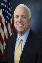 John McCain poster portrait with a smiling man in a dark pinstripe suit, yellow tie, and American flag backdrop.