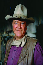 John Wayne poster portrait in a tan cowboy hat, neckerchief, brown vest, and purple shirt against a dark backdrop.