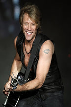Jon Bon Jovi wall art print captures the smiling rocker playing a black guitar in a sleeveless black leather vest.