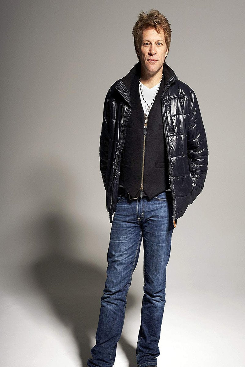 Jon Bon Jovi wall art print features a full-length studio portrait in a black puffer jacket, dark vest, and blue jeans.