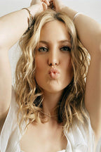 Kate Hudson poster portrait with wavy blonde hair, raised arms, bracelets, white blouse, and puckered lips against a pale background.