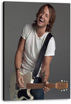Keith Urban canvas wall art print features the laughing guitarist with long hair, tattoos, and a cream electric guitar on gray.