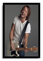 Keith Urban framed wall art print depicts the joyful musician playing a cream electric guitar, set in a glossy black frame.