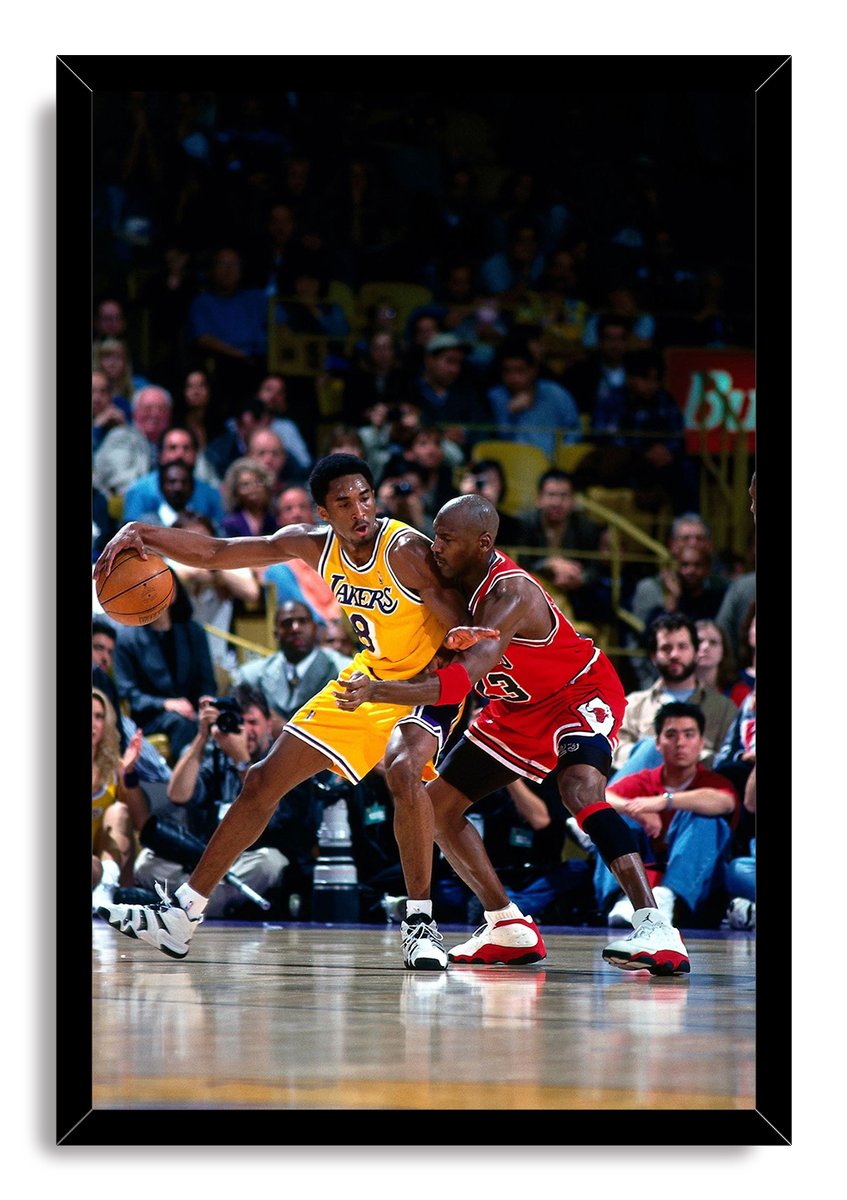 Kobe Bryant and Michael Jordan framed wall art print depicts Bryant handling the basketball in a yellow Lakers jersey against Jordan in a red Bulls uniform.