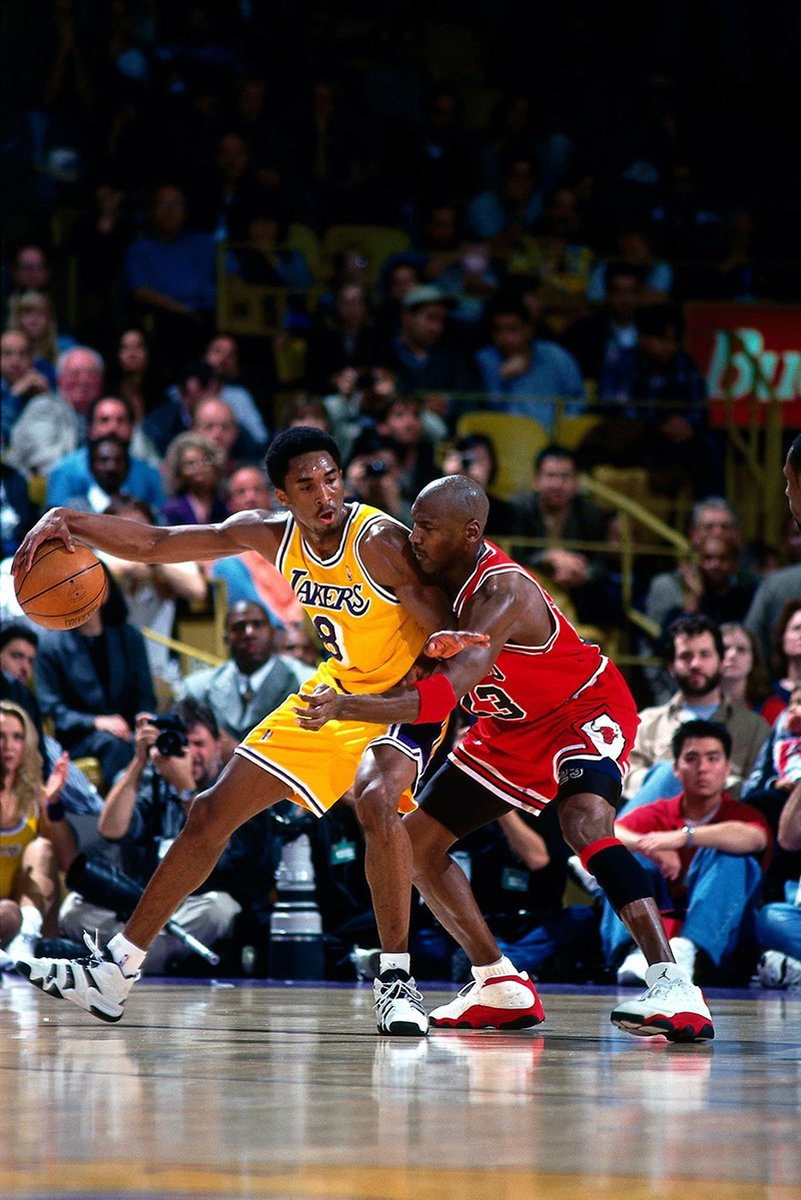 Kobe Bryant and Michael Jordan basketball poster captures Bryant dribbling in a yellow Lakers number 8 jersey as Jordan defends in red, before a packed crowd.