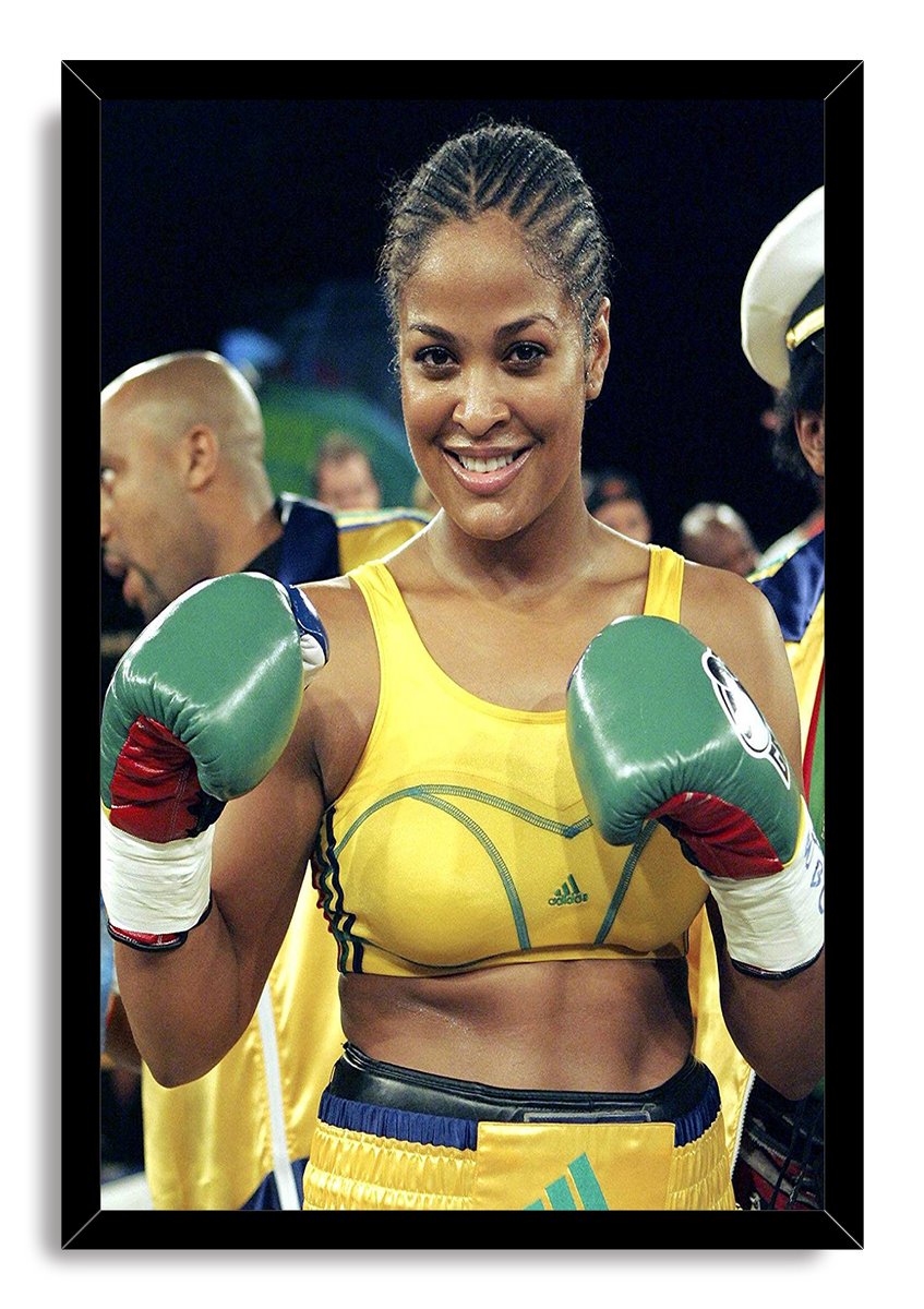 Laila Ali framed wall art print portrays the boxer smiling with green gloves raised, yellow boxing attire, and ringside figures behind her.