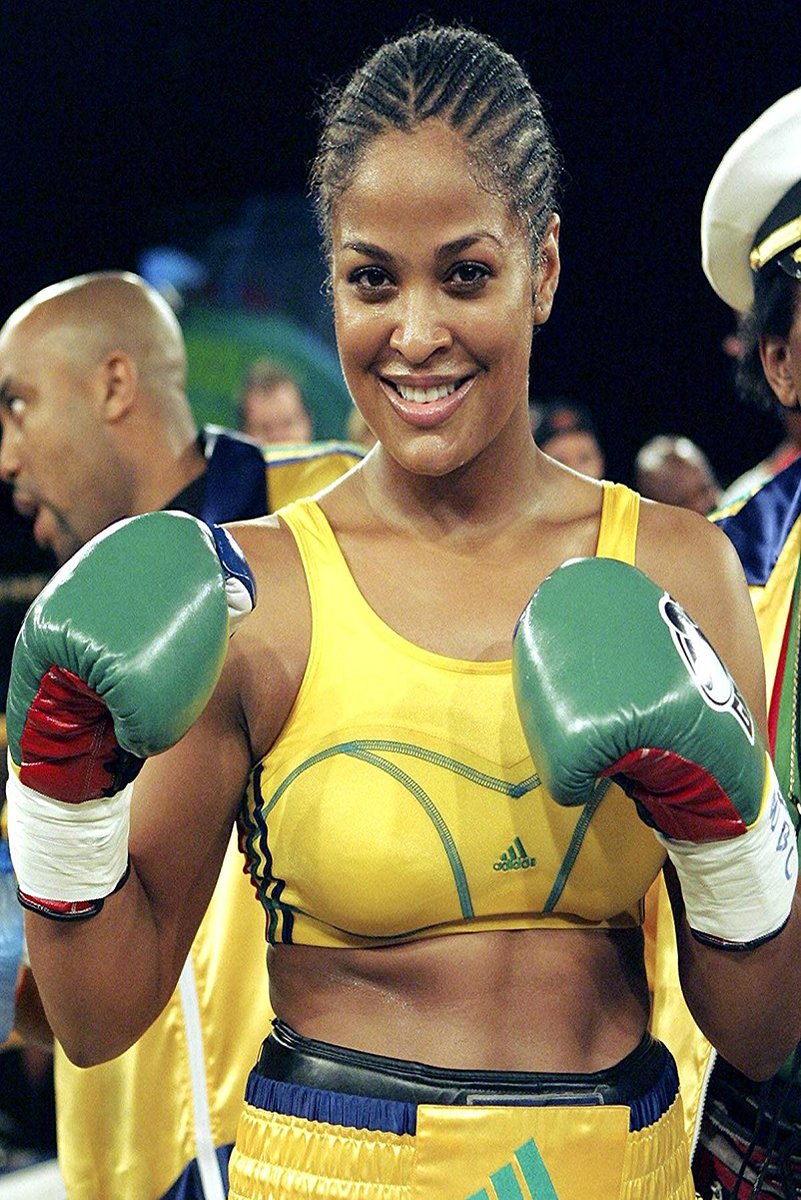 Laila Ali poster features the smiling boxer in a yellow uniform with raised green gloves amid her ringside team.