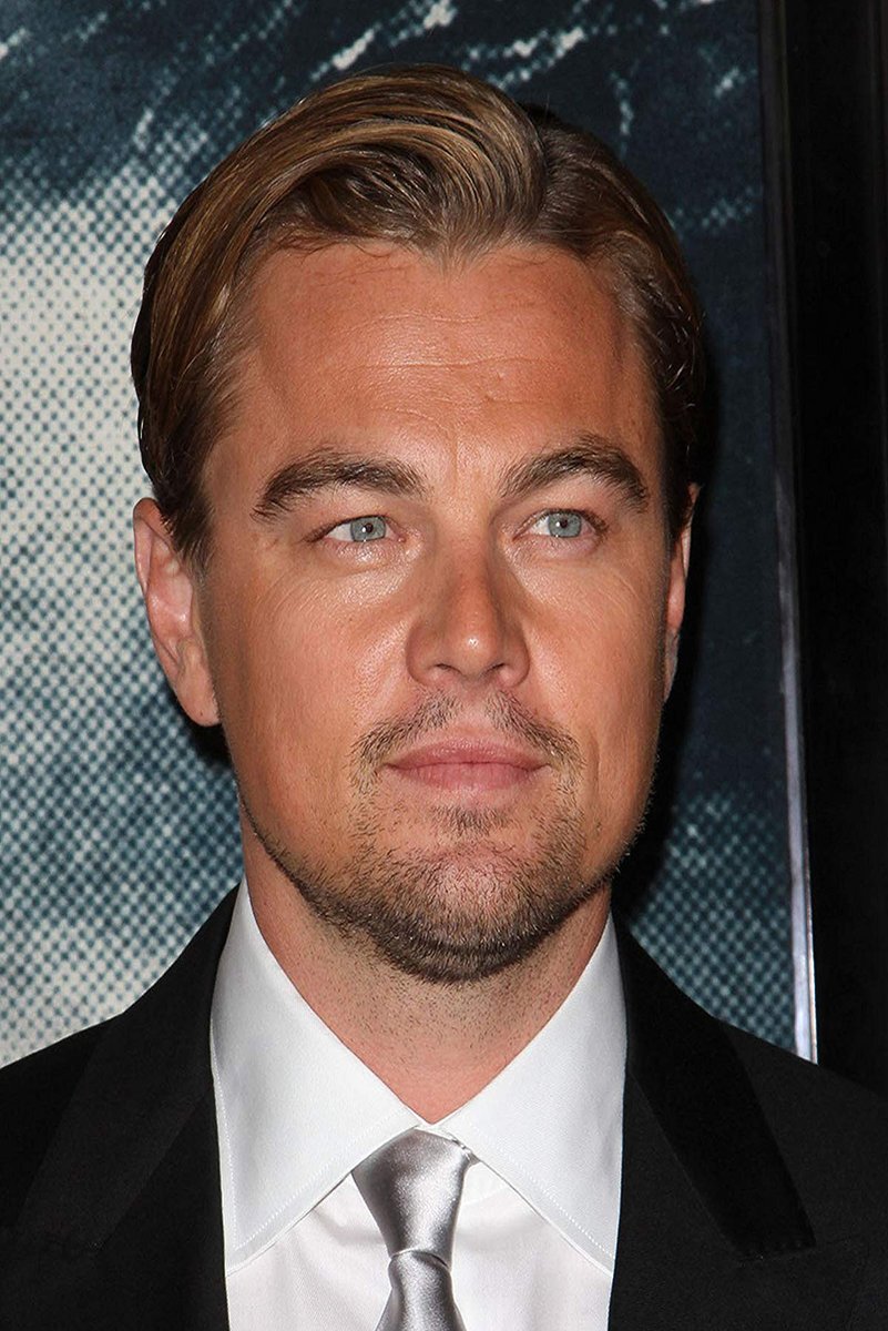 Leonardo DiCaprio poster portrait in a black suit, white shirt, and silver tie against a dark blue patterned backdrop.