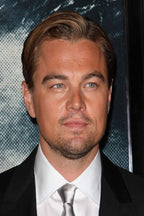 Leonardo DiCaprio poster portrait in a black suit, white shirt, and silver tie against a dark blue patterned backdrop.