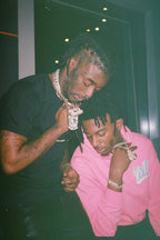 Lil Uzi Vert and Playboi Carti poster features two men looking down in a dark interior, wearing chains and black and pink clothing.
