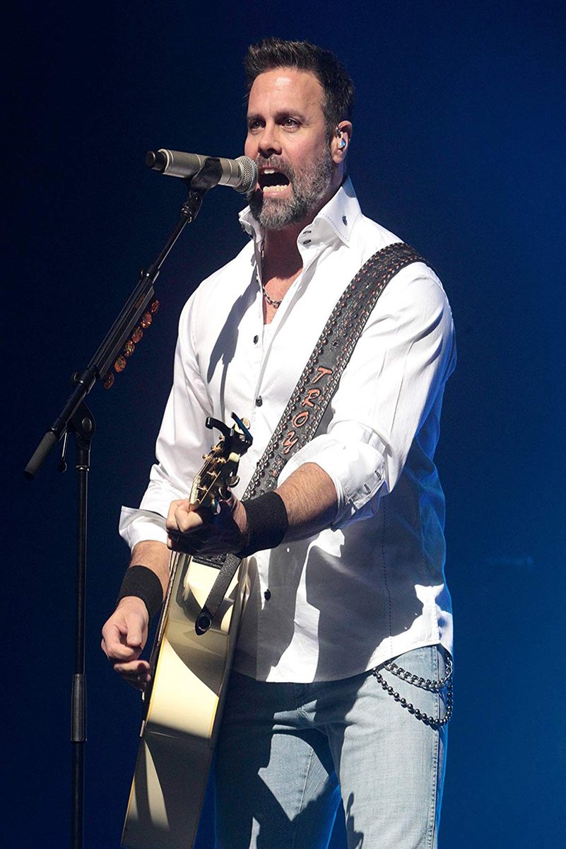 Male singer wall art print captures a bearded performer singing into a microphone while holding an acoustic guitar on a deep blue stage.