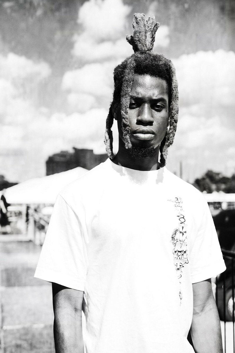 Black-and-white wall art print of a serious man in a white T-shirt, with tall dreadlocks against a cloudy outdoor sky.