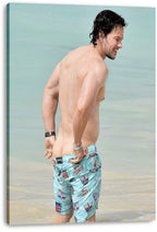 Mark Wahlberg canvas wall art print features the actor standing in pale blue seawater in colorful patterned swim shorts.