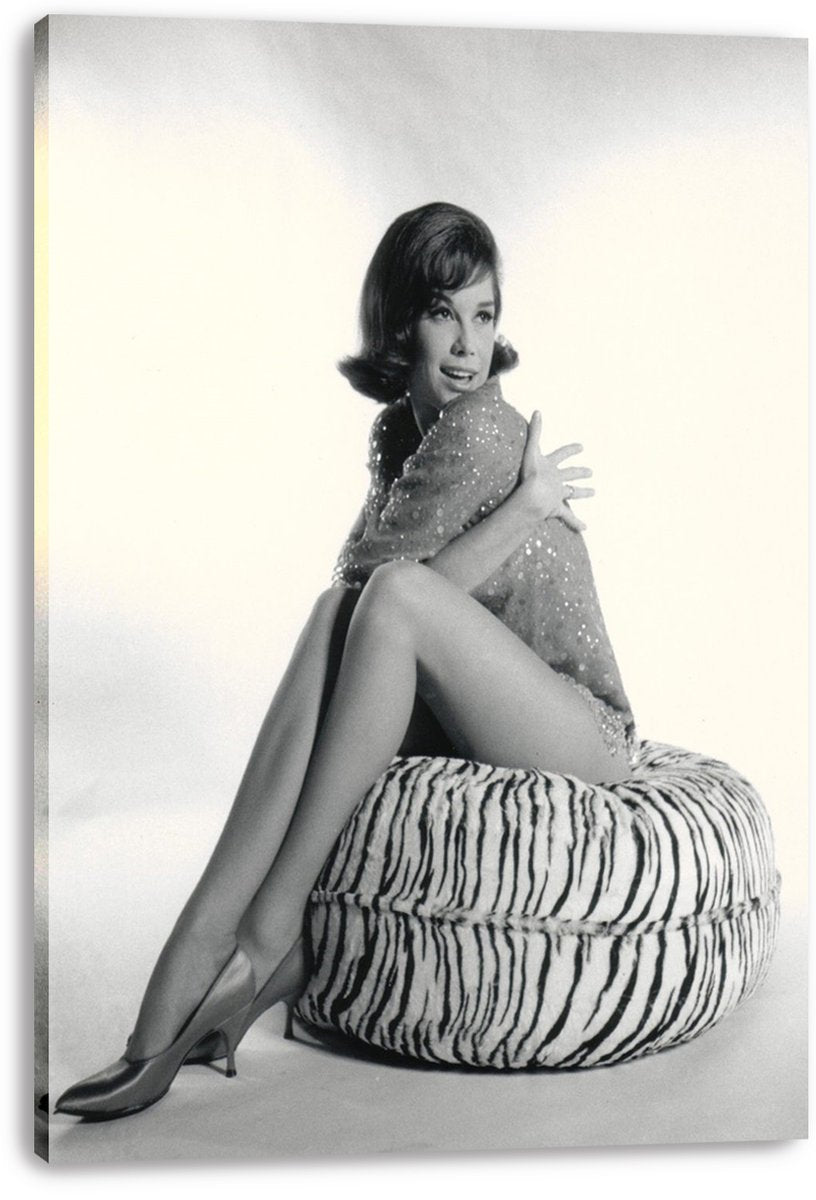 Mary Tyler Moore canvas wall art print displays a monochrome portrait of her sitting on a zebra-striped ottoman in a sparkling outfit.