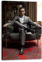 Moriarty canvas wall art print features Andrew Scott in a gray suit seated in a leather chair before shelves and curtains.
