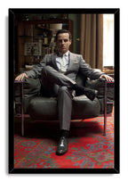 Moriarty framed wall art print portrays Andrew Scott seated cross-legged in a leather armchair, with a black border and red rug.