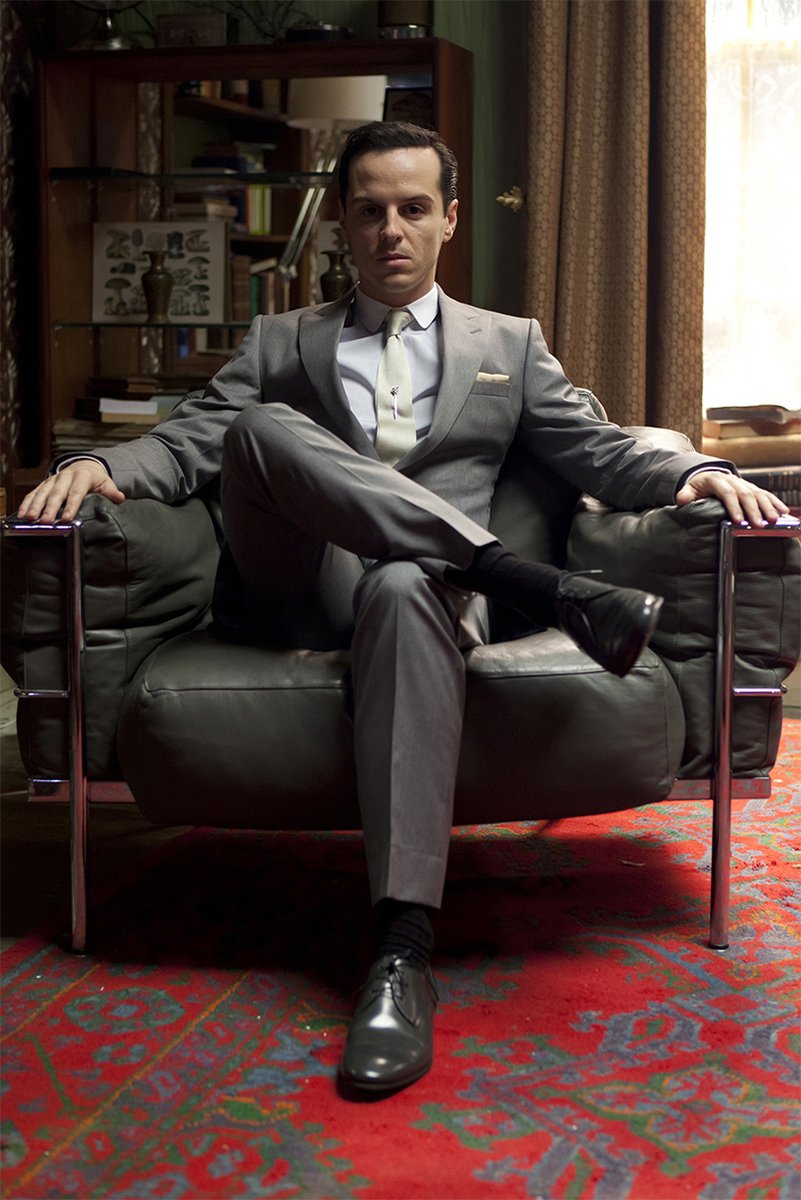 Moriarty poster depicts Andrew Scott seated in a dark leather armchair, wearing a gray suit on a red patterned rug.