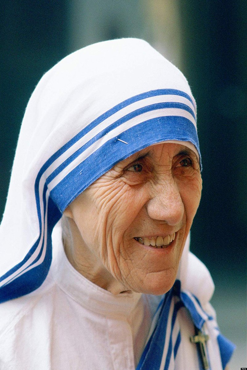 Mother Teresa poster portrait with her smiling in a white headscarf with blue stripes against a soft dark background.