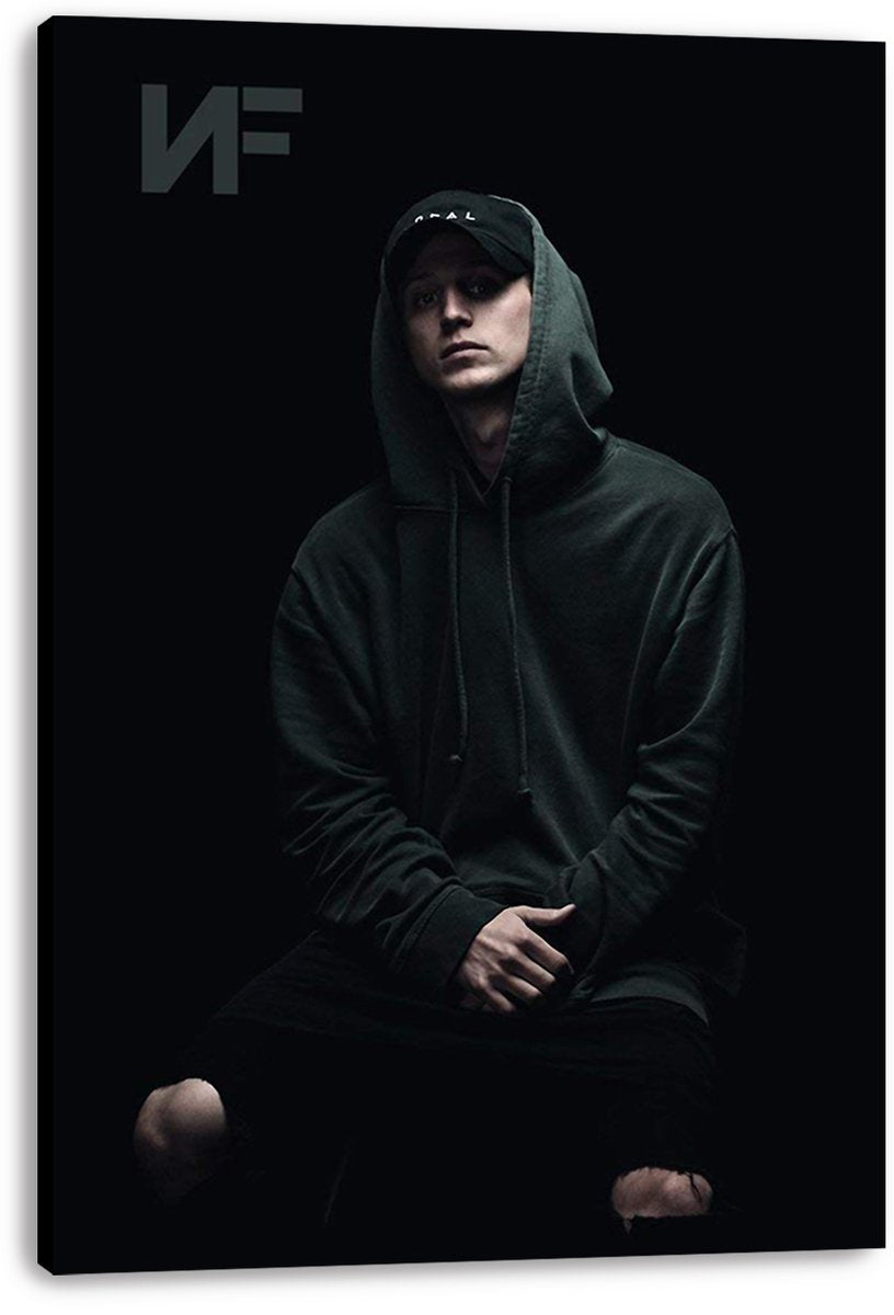 NF canvas wall art print presents a moody portrait of the rapper seated in a hoodie and cap against a deep black backdrop.