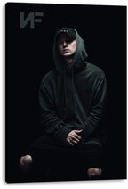 NF canvas wall art print presents a moody portrait of the rapper seated in a hoodie and cap against a deep black backdrop.
