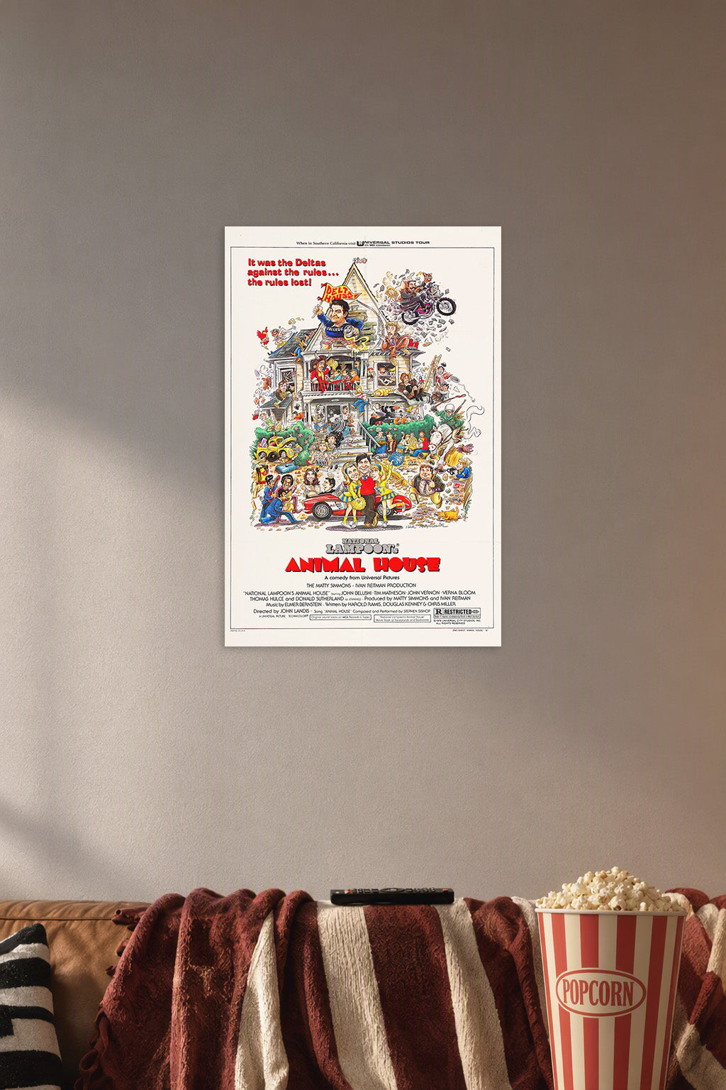 National Lampoon's Animal House Movie Poster in a cozy movie room above a brown sofa with popcorn.