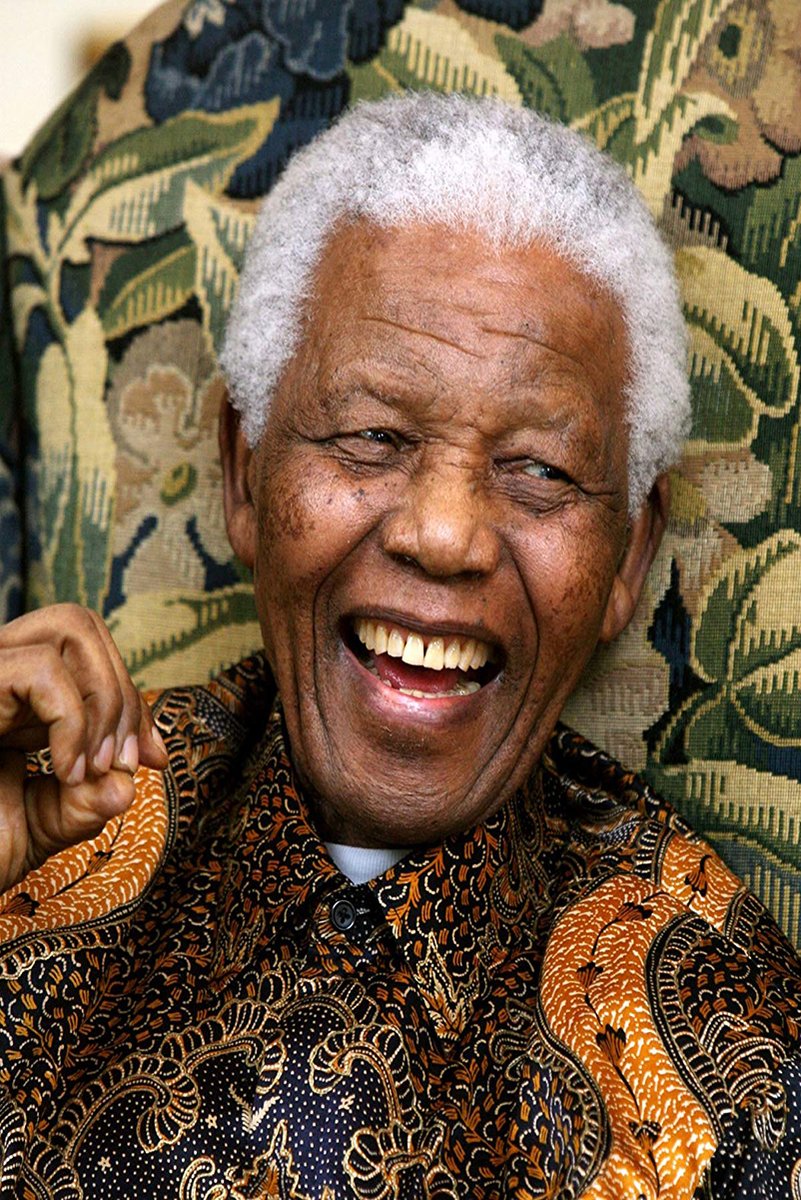 Nelson Mandela poster features a close-up of him laughing in a black and orange patterned shirt before floral upholstery.