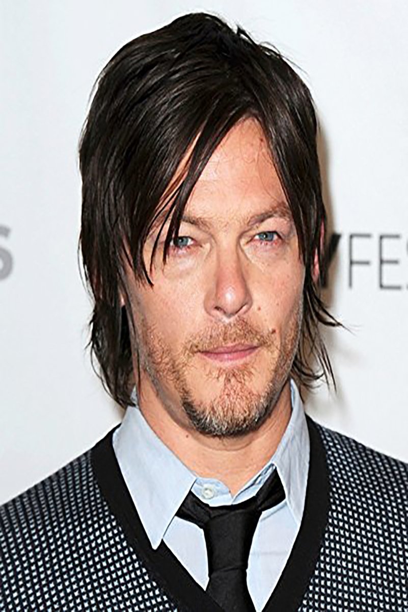 Norman Reedus poster portrait with dark layered hair, blue eyes, light shirt, black tie, and patterned jacket.