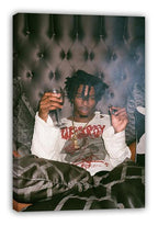 Playboi Carti wall art canvas featuring the rapper reclining with a wine glass, white shirt, gold chains, and dark patterned blanket.