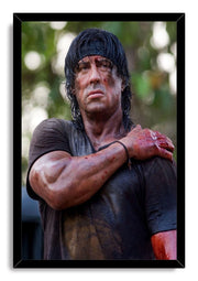 Rambo framed wall art print featuring Sylvester Stallone with a wounded arm and intense gaze, set in a black mitered frame.
