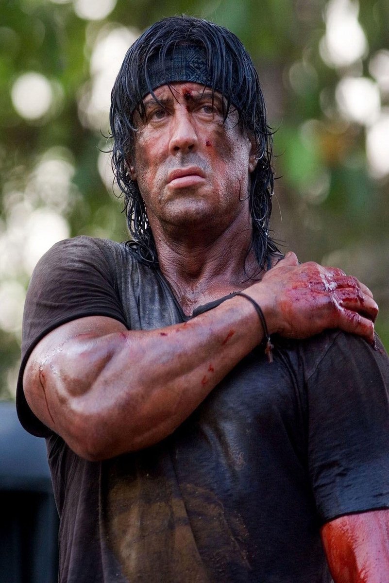 Rambo wall art print featuring Sylvester Stallone with wet dark hair, a bloodied arm, and a stern expression against green foliage.