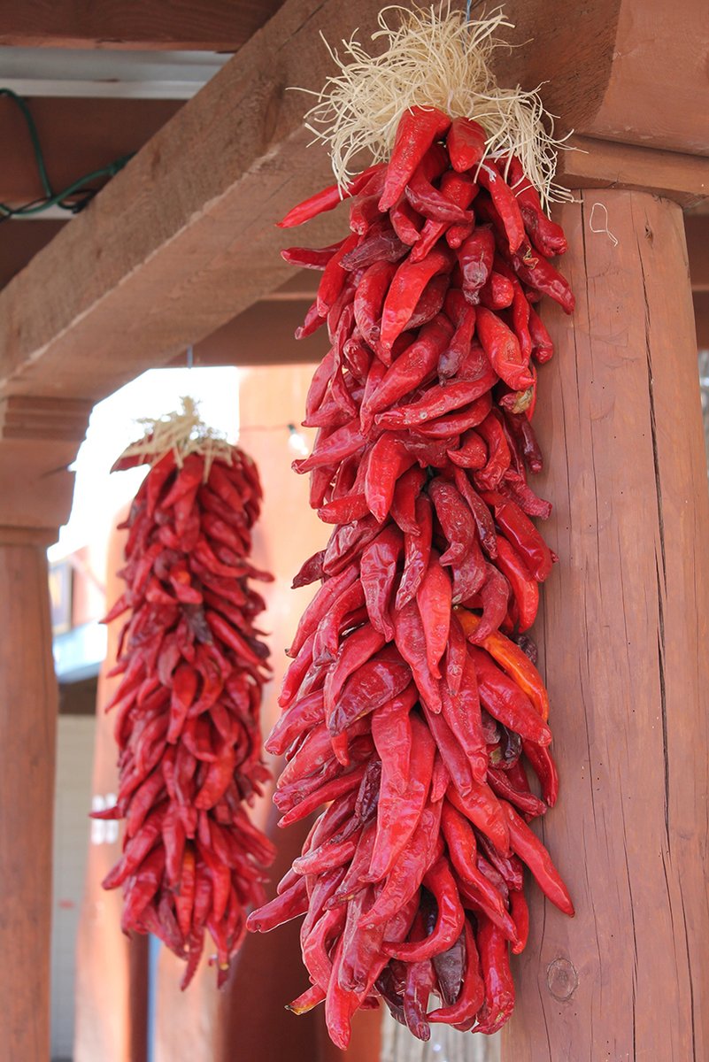 Red chili ristras wall art print featuring two bundles of dried red peppers hanging from rustic wooden beams.