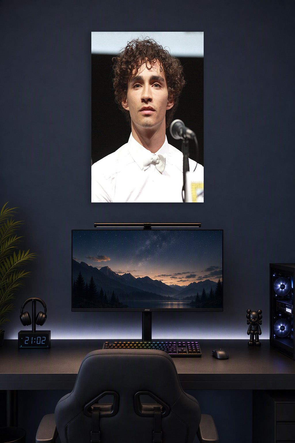 Robert Sheehan in a gaming desk setup above a monitor.