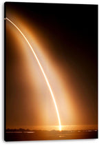 Rocket launch canvas wall art print displays a curved golden light trail over a dark silhouetted landscape, with visible wrapped edges.