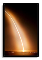 Rocket launch framed wall art print features a luminous arcing trail above an orange horizon, presented in a slim black frame.