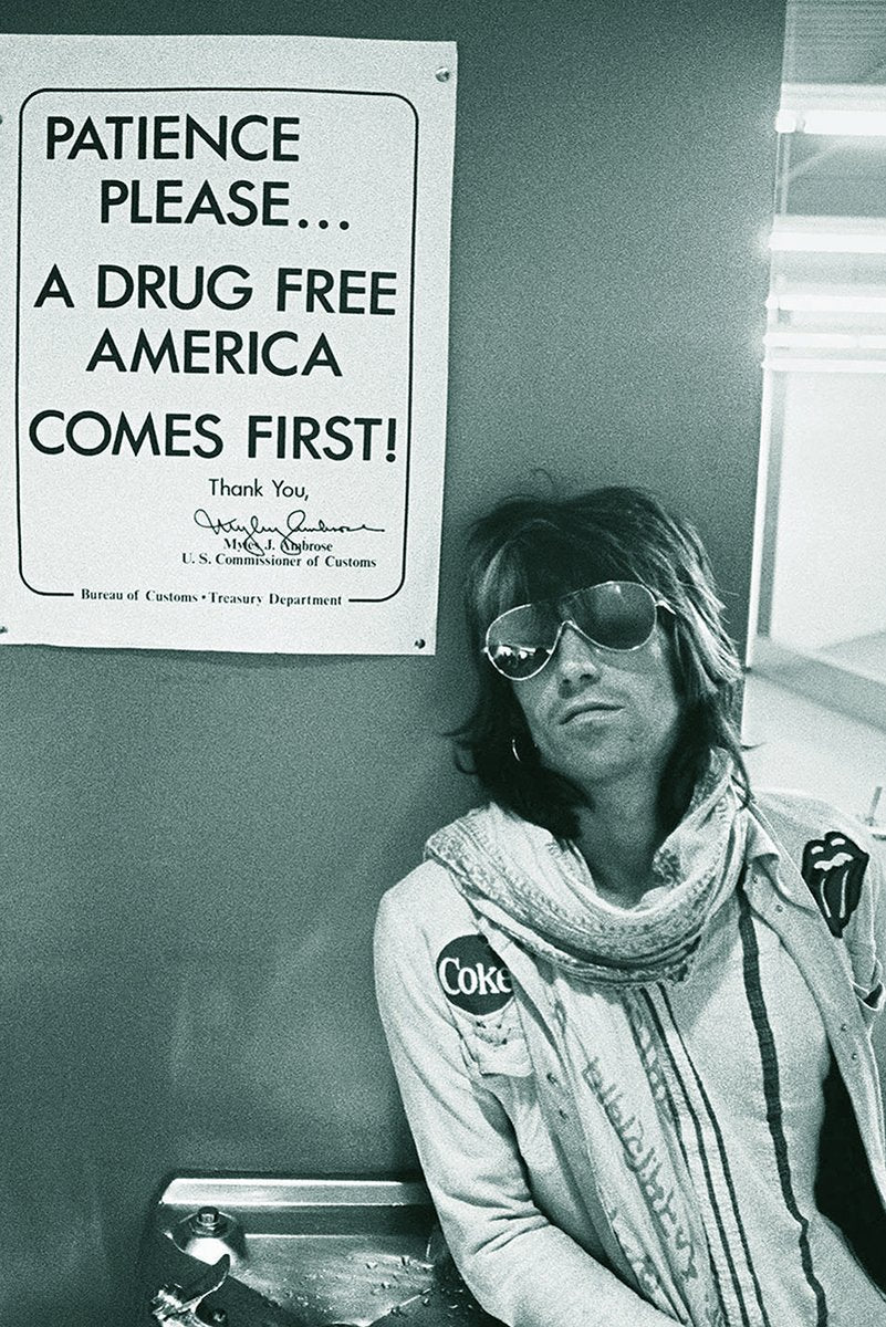 Keith Richards poster featuring a monochrome candid portrait of the musician in sunglasses, scarf, and patched jacket by a wall sign.